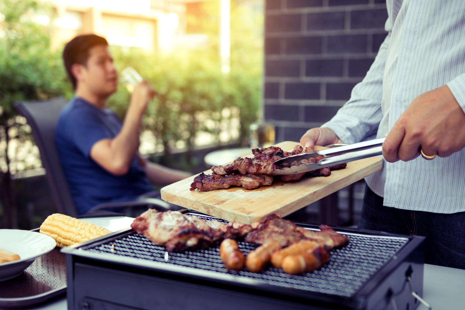 Asian men are pinching pork on a wooden cutting board and holding it to friends who are celebrating in the back.<br />